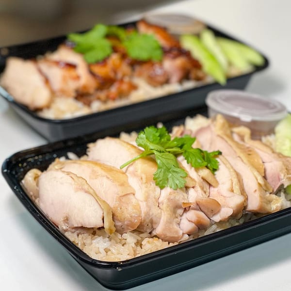 Two black takeout containers of Gai Kitchen's Thai chicken and rice, garnished with cilantro and cucumber.