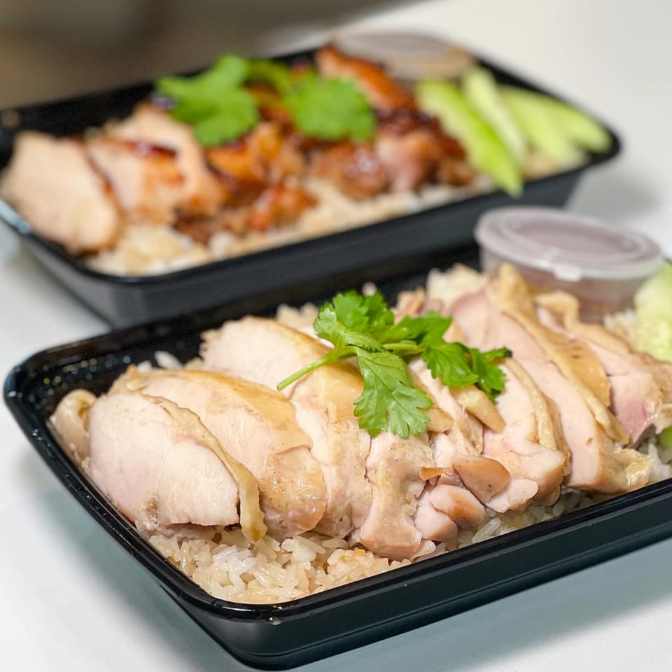 Two black takeout containers of Gai Kitchen's Thai chicken and rice, garnished with cilantro and cucumber.