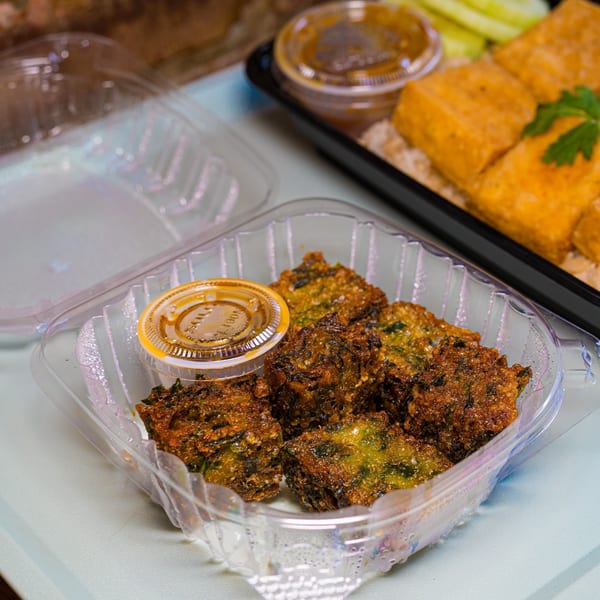 Gai Kitchen's crispy fried vegetable fritters with dipping sauce in a clear takeout container.