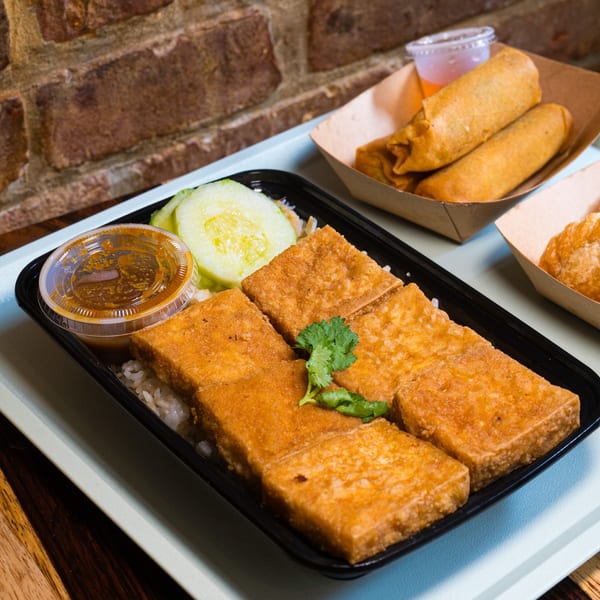Gai Kitchen's fried tofu with rice, cucumber, sauce, and two spring rolls on a tray.