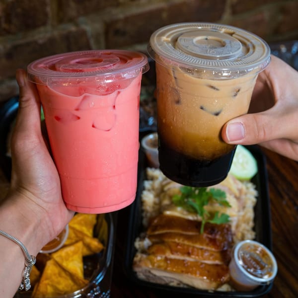 Hands holding a pink drink and an iced coffee over Thai food from Gai Kitchen.