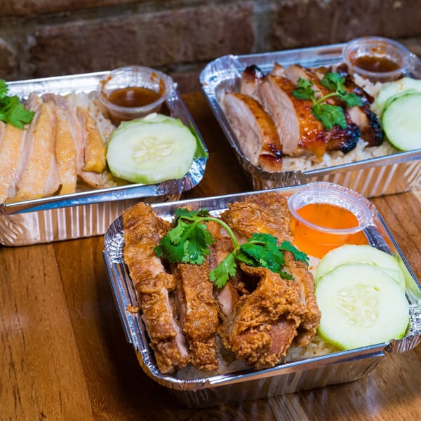 Three foil containers of Gai Kitchen's Thai chicken and duck rice dishes with sauces and cucumbers.